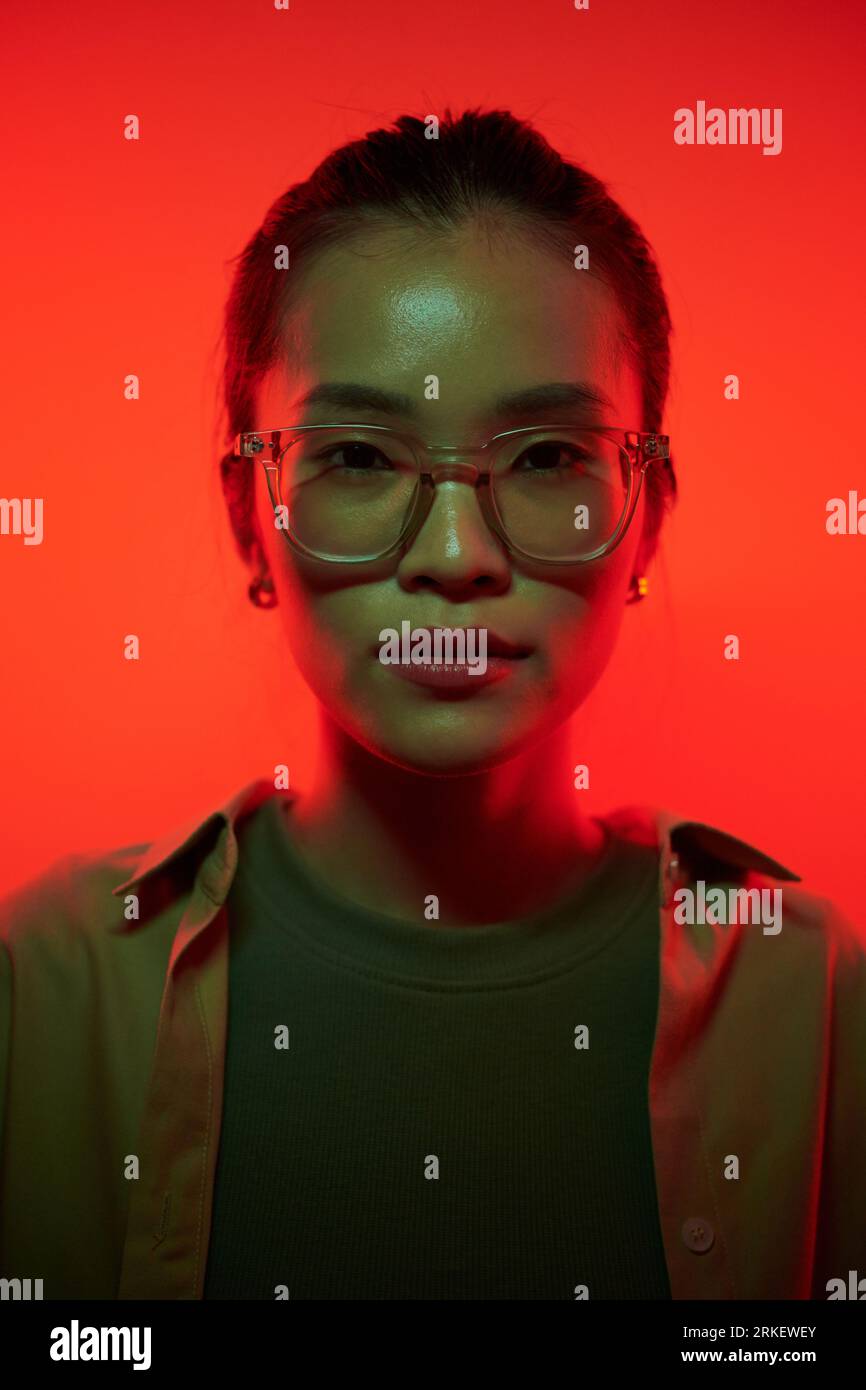Porträt einer jungen Asienfrau in rotem Licht stehender Brille Stockfoto