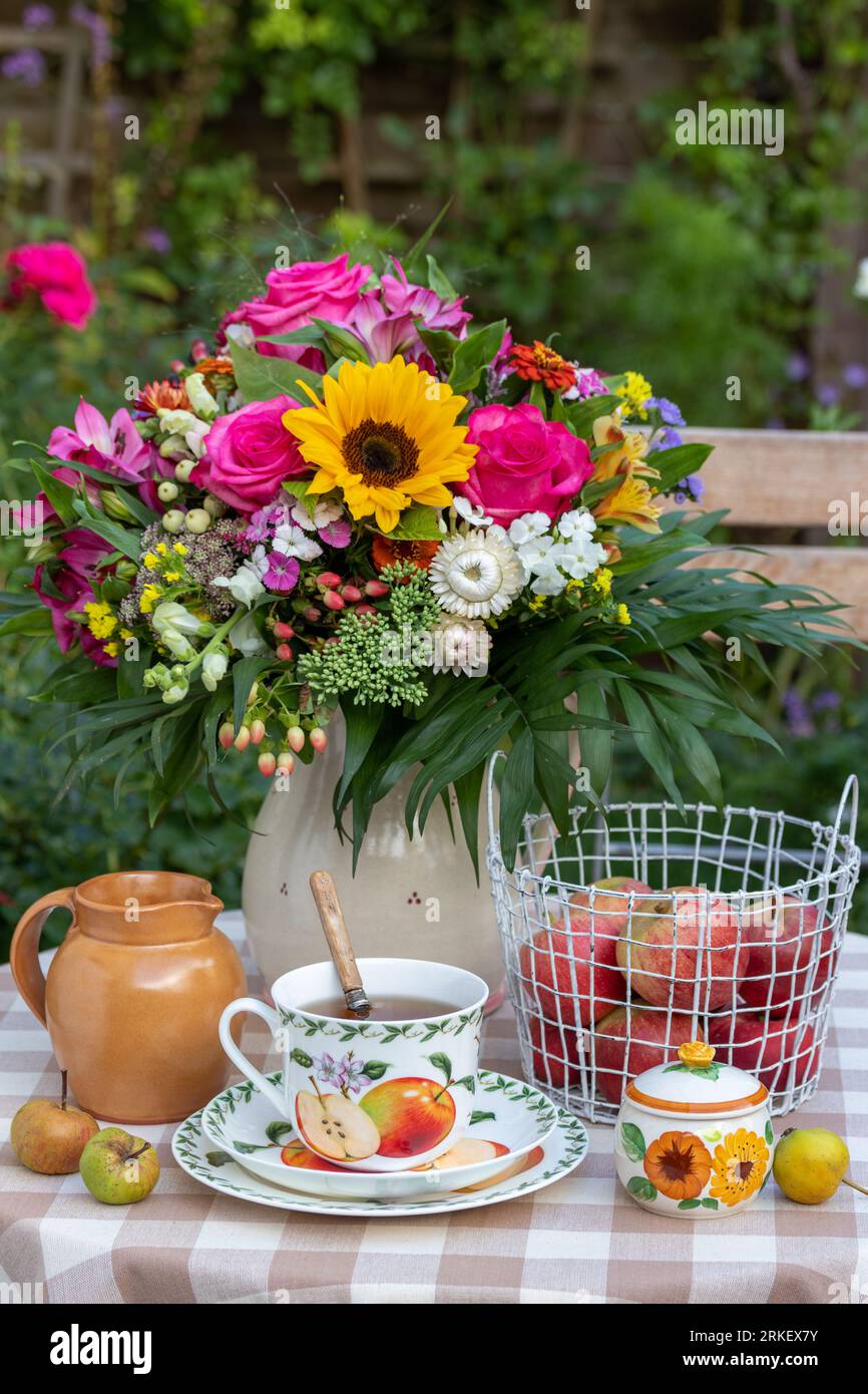 Tischdekoration mit einer Tasse Tee, Äpfeln im Korb und einem Blumenstrauß im Sommer Stockfoto