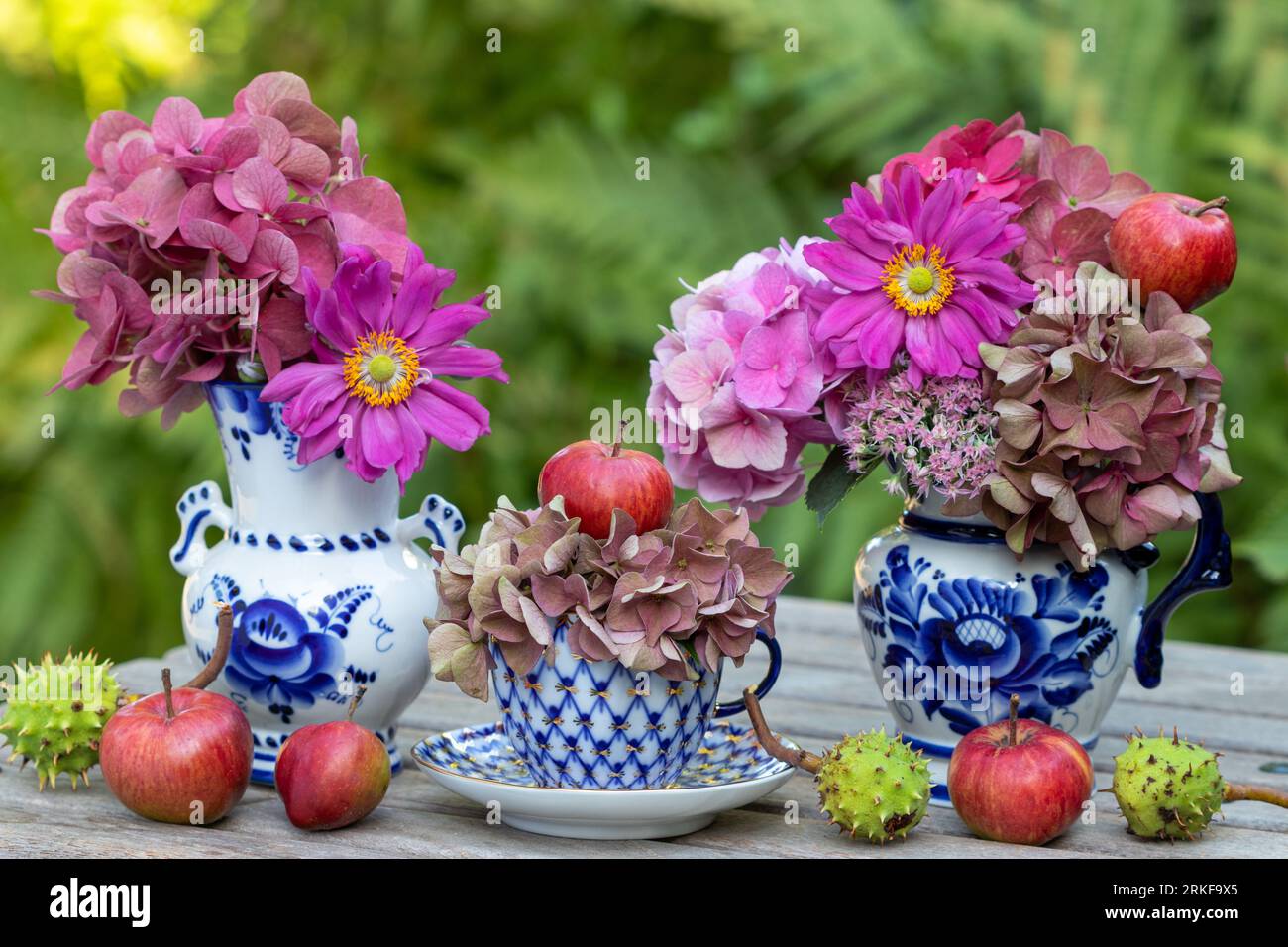 blumenarrangement mit Vintage-Porzellan, Äpfeln und Sträußen mit rosa Hortensienblüten und japanischen Anemonen Stockfoto