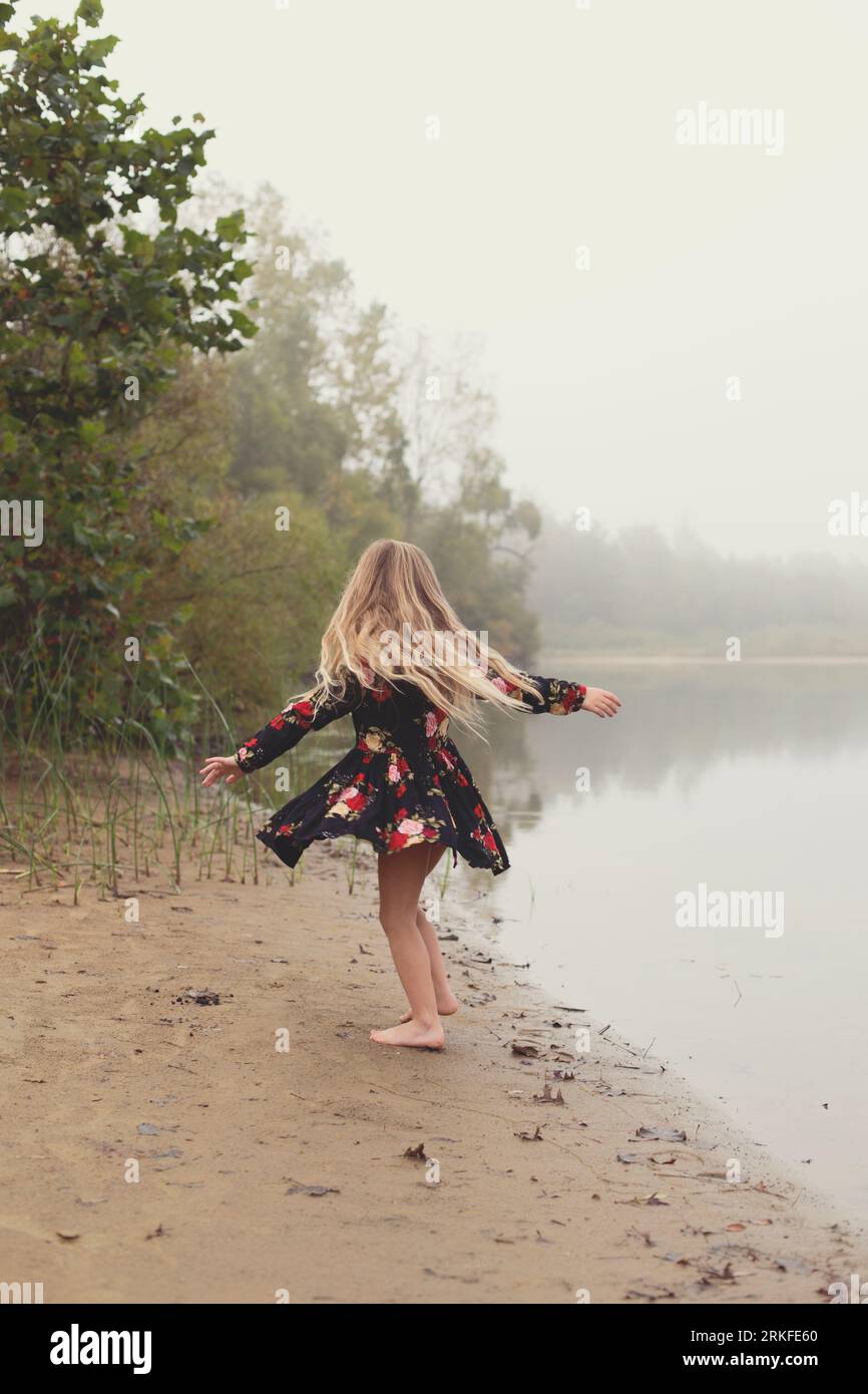 Gesichtsloses Mädchen wirbelt und dreht sich an einem nebligen See Stockfoto