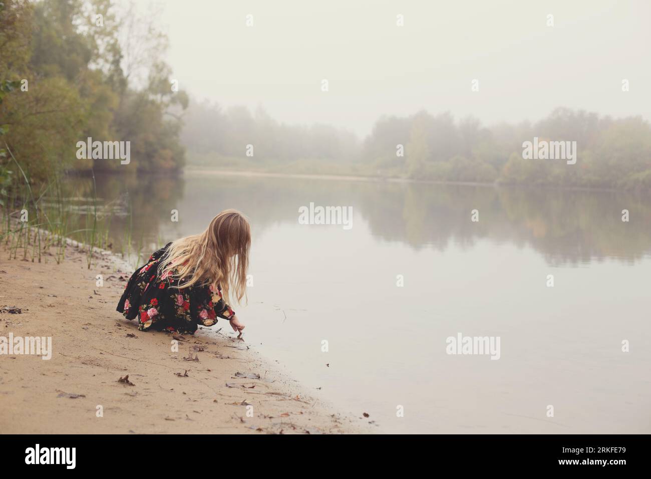 Ein nebliger Blick auf den See am Morgen mit einem kleinen Mädchen mit wilden Haaren Stockfoto