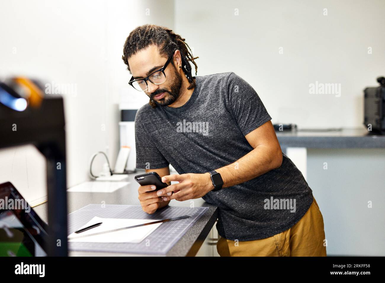 Confident businessman using smart phone while standing by table in office Stockfoto