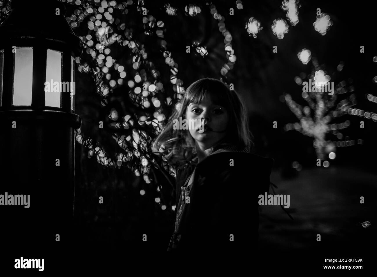 Junge Mädchen in der Nacht in schwarz-weiß mit Bokeh und weihnachtsbeleuchtung Stockfoto