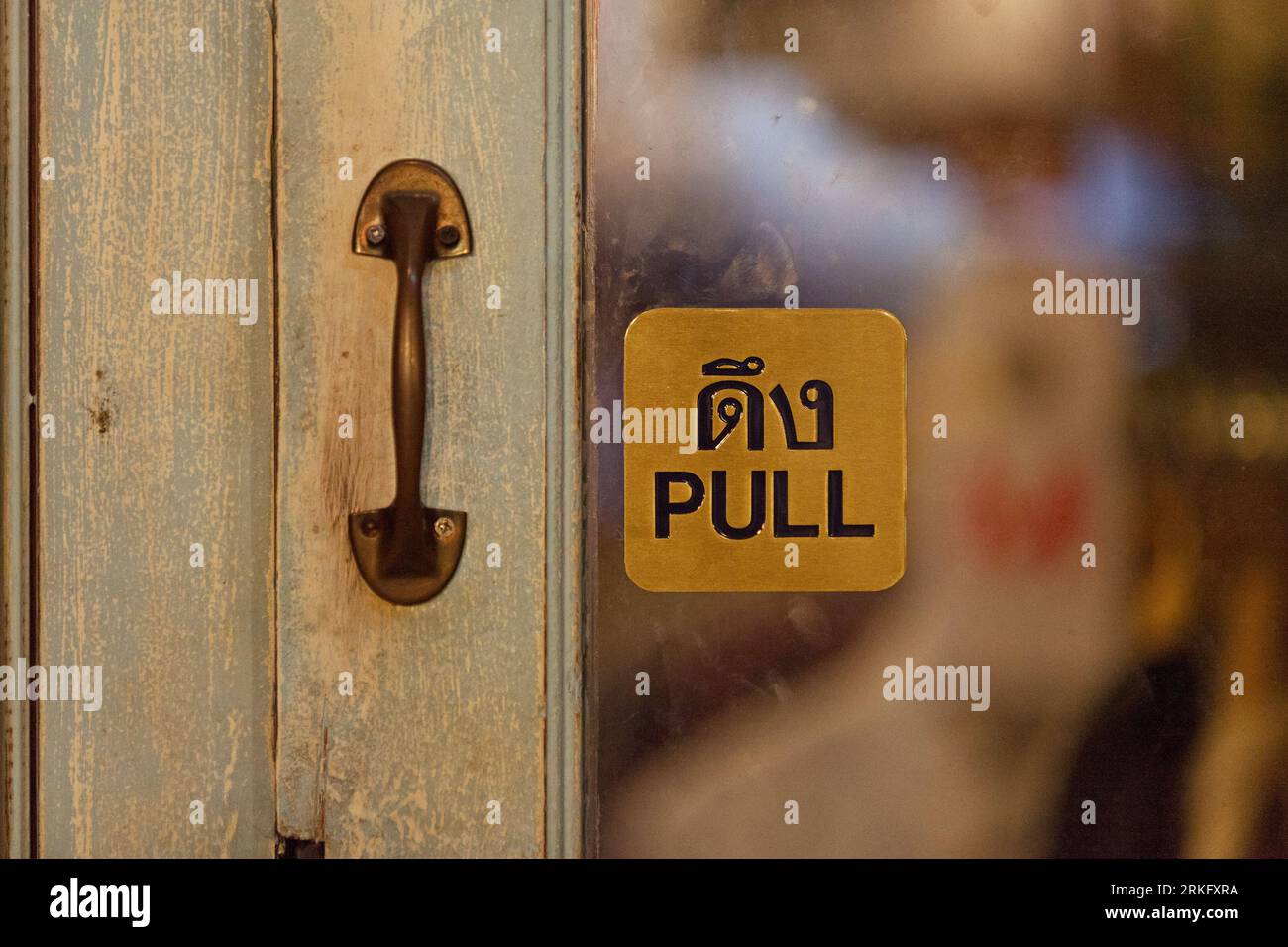 Halten Sie sich an der Tür eines Geschäfts fest und sagen Sie auf Thailändisch und Englisch „Pull“. Stockfoto