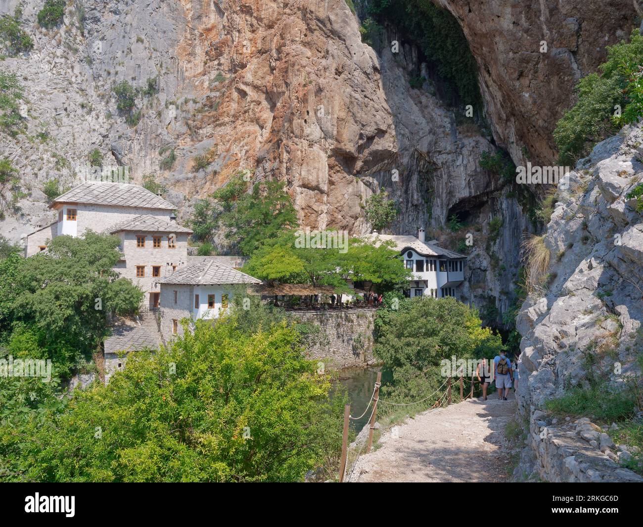 Das Blagaj-Kloster (oder Blagaj Tekija) am Fluss Buna mit Touristen auf einem Pfad im Vordergrund in der Nähe von Mostar, Bosnien und Herzegowina, 24. August 2023. Stockfoto