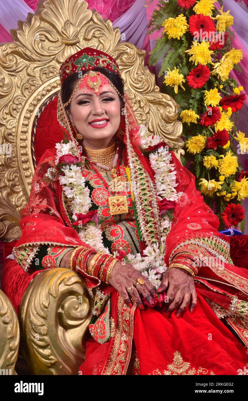 Eine fröhliche, lächelnde nepalesische Braut, die ein rotes Saree und Goldschmuck trägt. Stockfoto