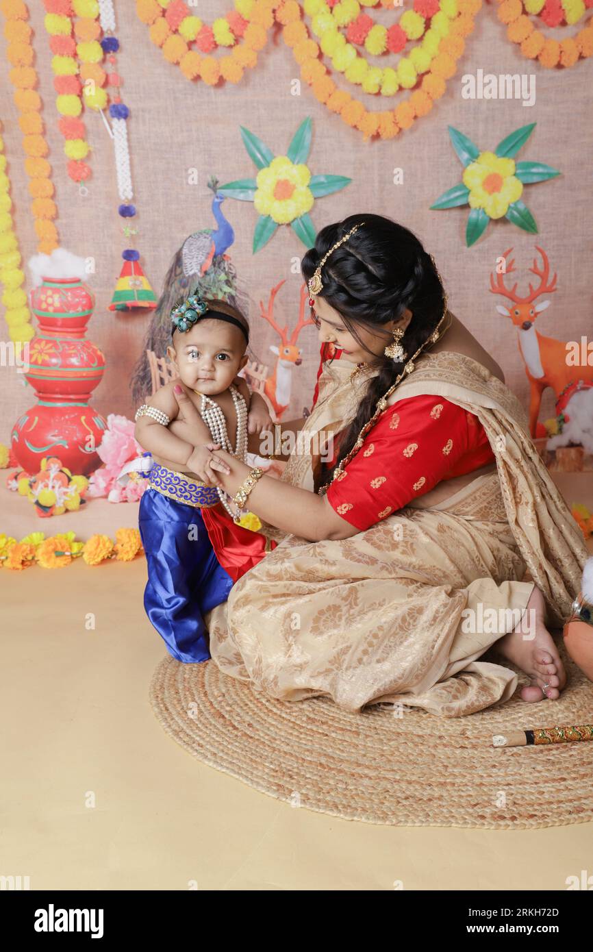 Janmashtami-Konzept. Mutter sitzt mit ihrem süßen Jungen, der als kleine krishna verkleidet ist. Stockfoto