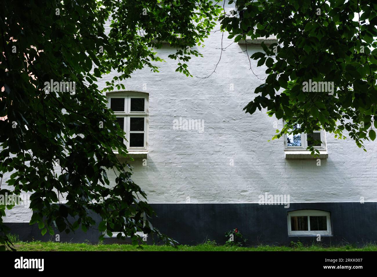 Dunkle Äste umrahmen die weißen Wände ländlicher Backsteinhäuser, bukolischer Hintergrund Stockfoto