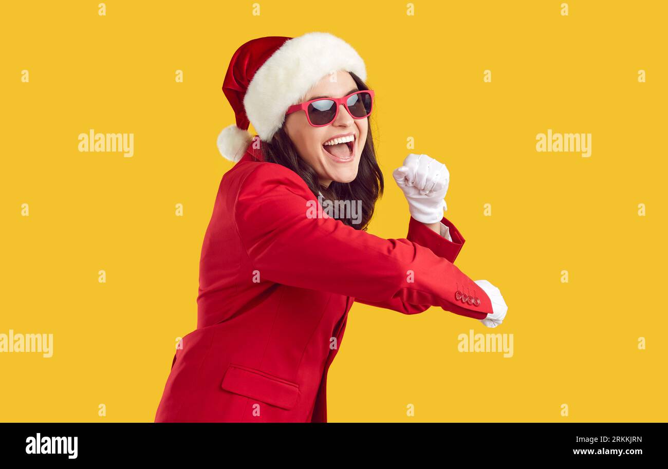 Fröhlich fröhlich brünette junge Frau im Weihnachtsmannstil, lustig tanzen auf gelbem Hintergrund. Stockfoto