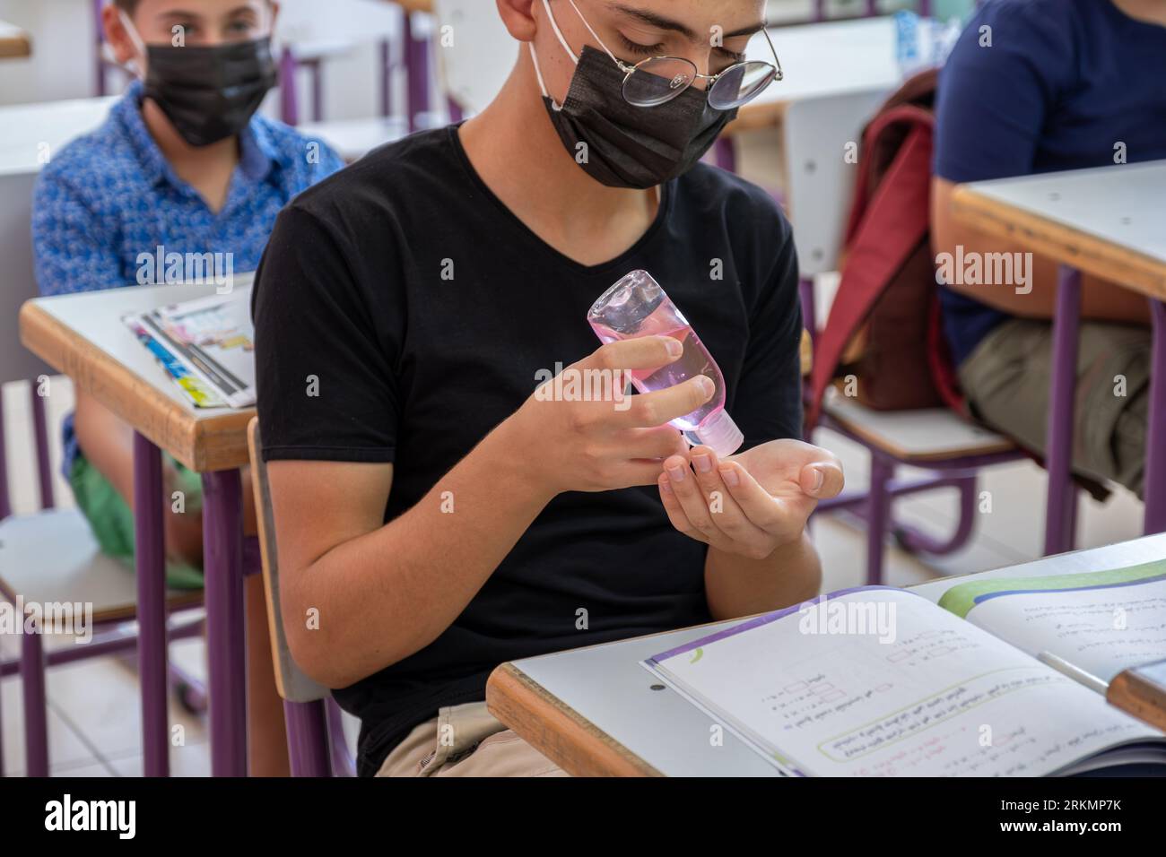 Teenager in der Schule, der seine Hände sterilisiert, während er eine Gesichtsmaske trägt, um Infektionen zu verhindern Stockfoto