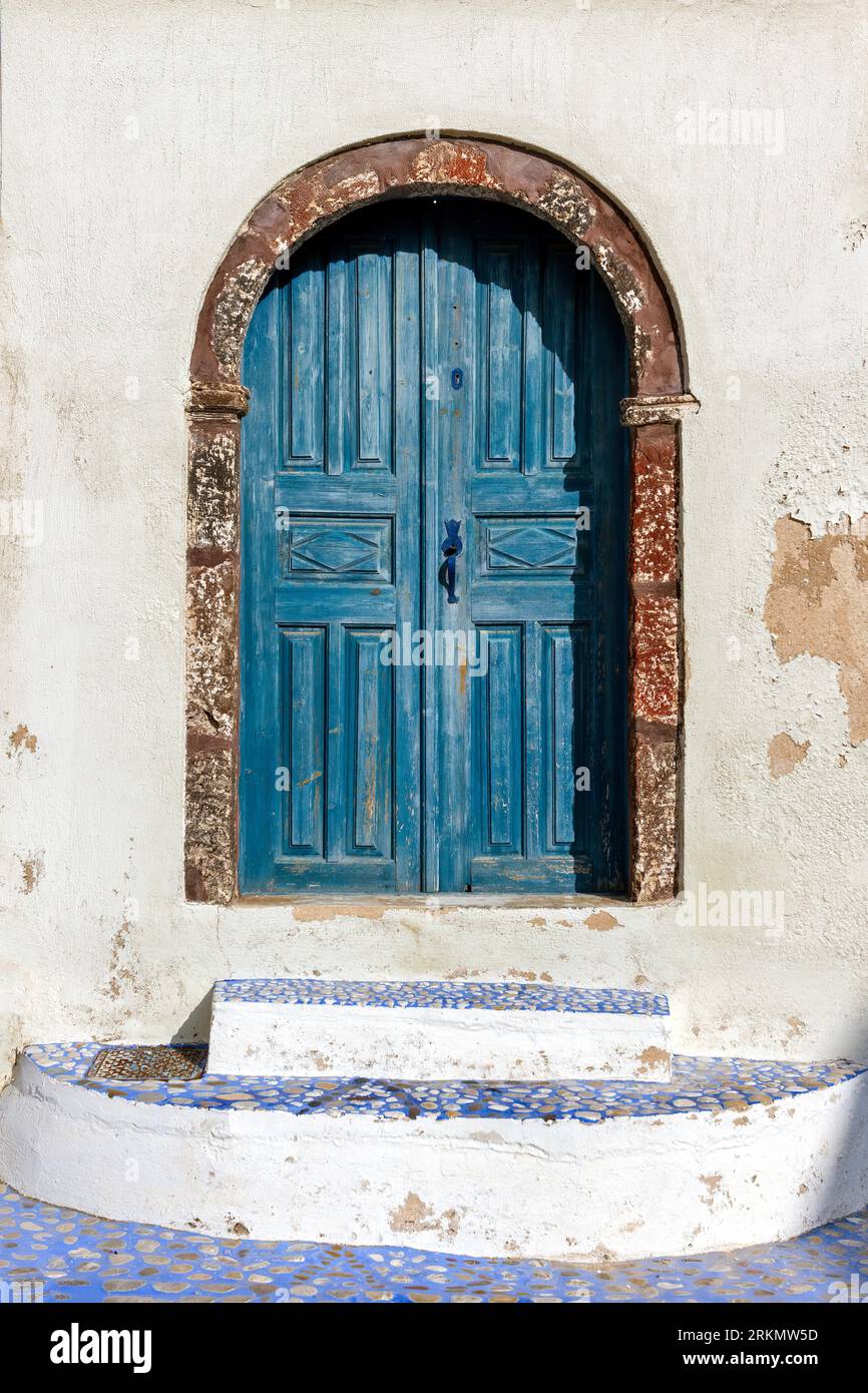 Traditionelle alte Holztür in bläulich-grünlicher Farbe an einem alten Haus mit ockerfarbenen Wänden und Steinschwelle, im Pyrgos Dorf Santorini, Griechenland. Stockfoto