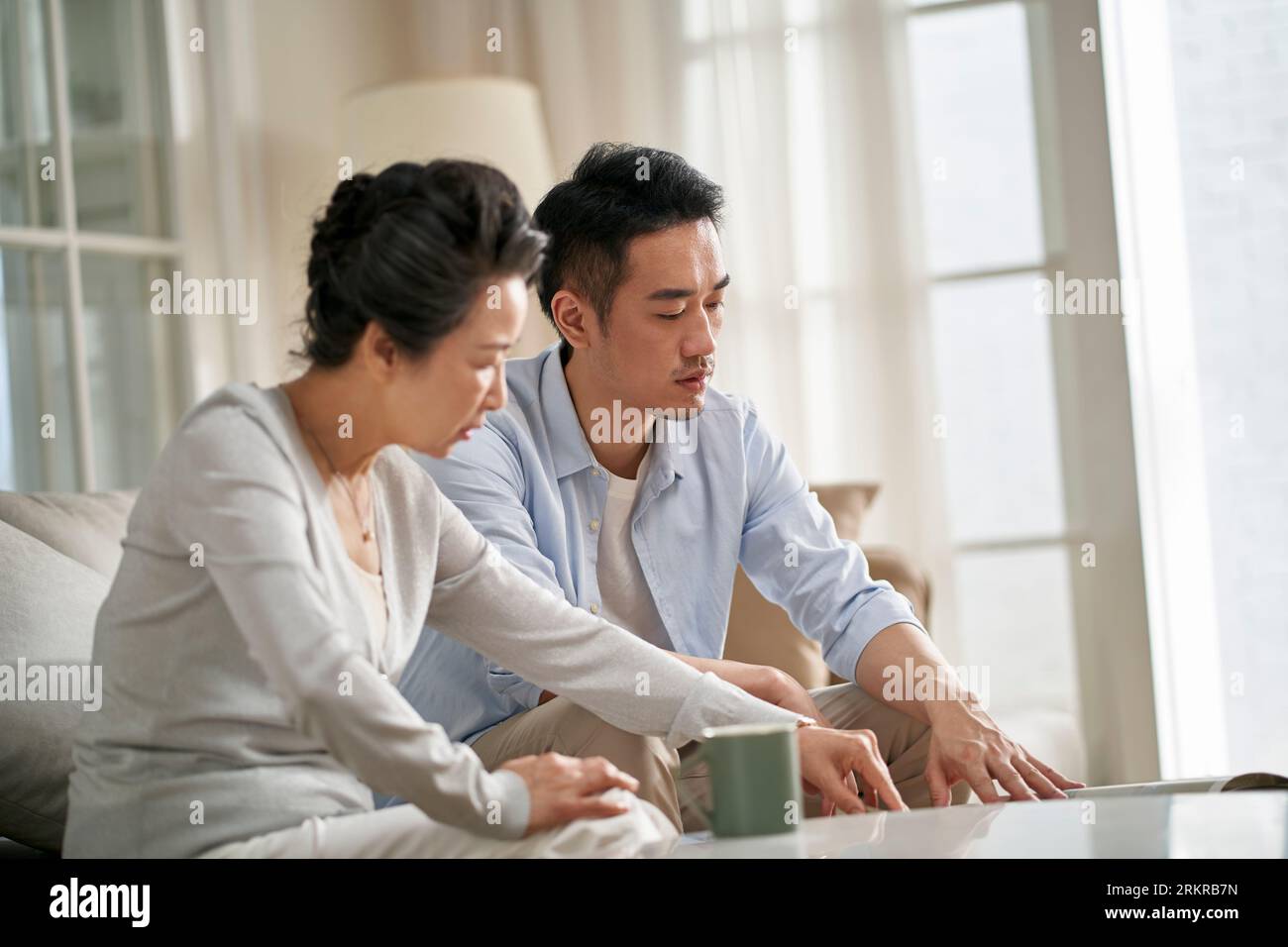 Ältere asiatische Mutter und erwachsener Sohn sitzen auf der Couch im Wohnzimmer zu Hause und unterhalten sich Stockfoto