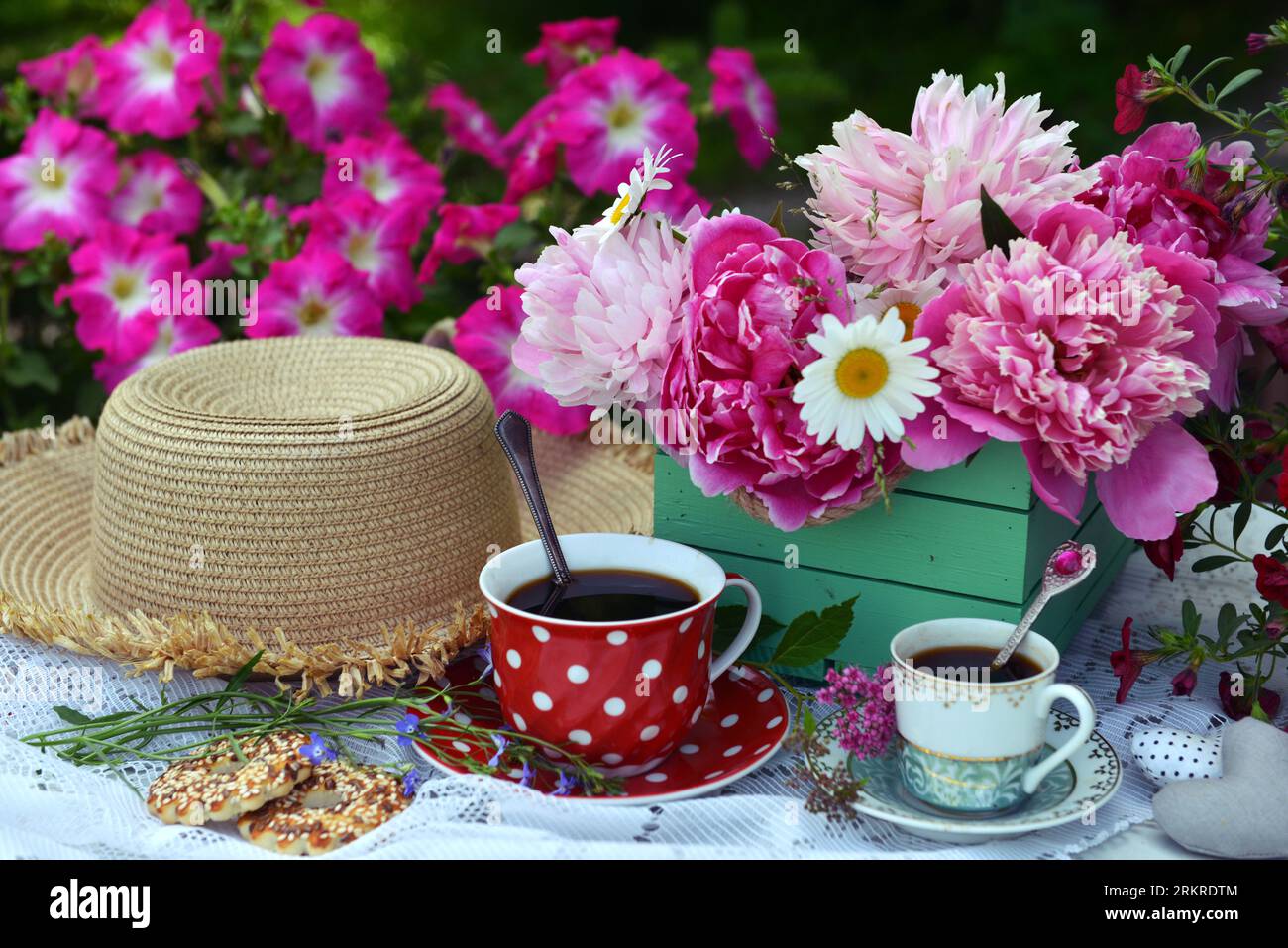 Wunderschönes Stillleben mit Pfingstrosenblüten, Teetasse und Hut auf dem Tisch. Romantische Grußkarte zum Geburtstag, Valentinstag, Muttertag Konzept. Summe Stockfoto