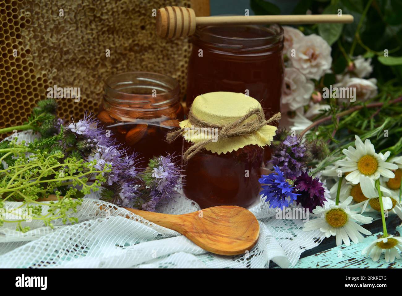 Stillleben mit natürlichem Honig im Glas, Dipper, Blumen und Stock auf hölzernem Hintergrund draußen. Landhaus Sommer ländlicher Hintergrund, Vintage-Konzept, er Stockfoto
