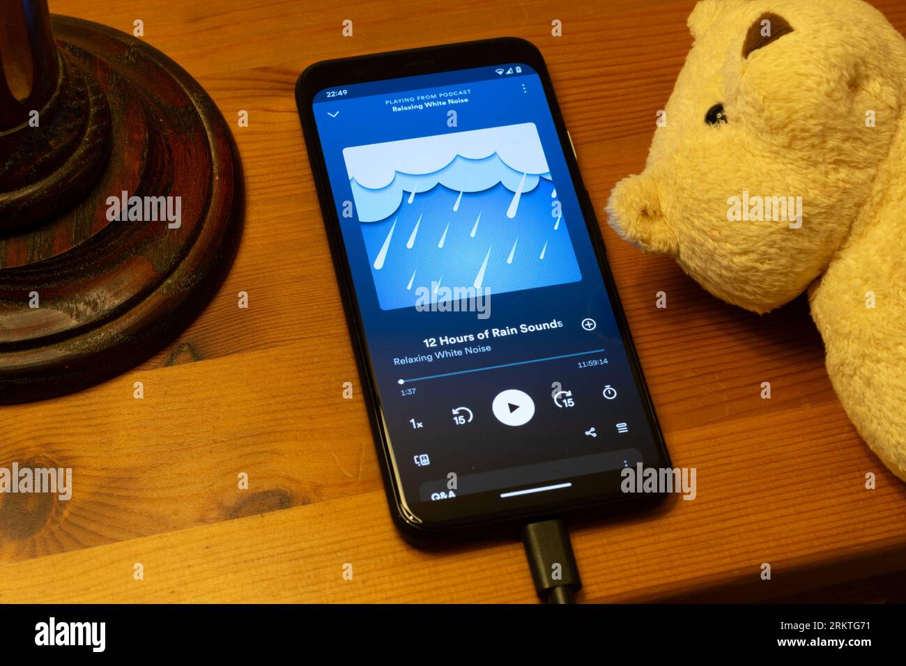 White Noise Podcast in der Spotify App. Android-Telefon zum Aufladen auf dem Nachttisch mit Teddybär und Lampe. Schlafhilfe. Stockfoto