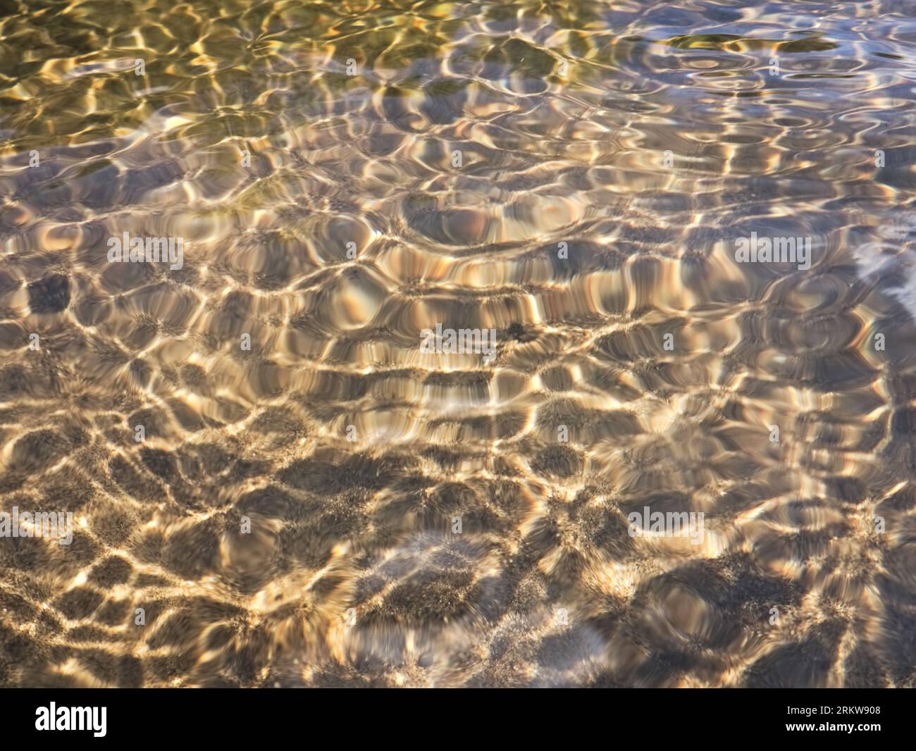 Reflexionen des Sonnenlichts in winzigen Wellen gegen den sandigen Boden eines flachen Flusses in hellen Tönen Stockfoto