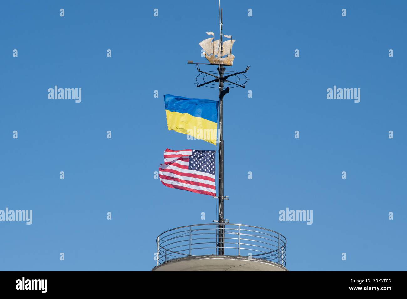 Die Flaggen der Ukraine und der USA flattern auf einem Fahnenmast vor einem blauen Himmel. Statussymbol. Ukrainische blaue und gelbe Flagge. Windtag im Freien. Stockfoto