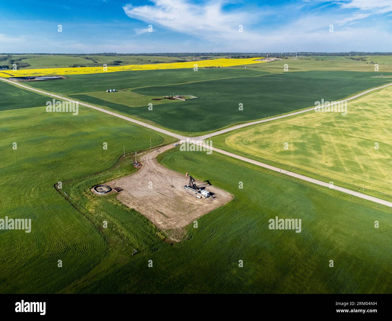 Luft-Öl- und Gasbrunnen an der Kreuzung mit Blick auf die landwirtschaftlichen Felder in den kanadischen Prärien in Alberta, Kanada. Stockfoto