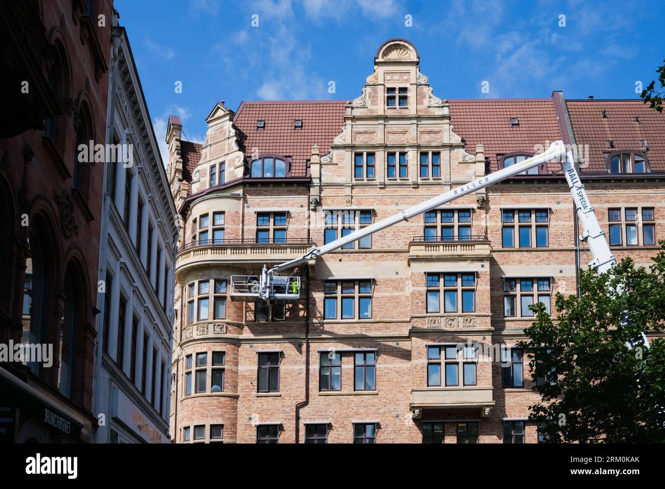 Malmö, Schweden - 8. August 2023: Ein Kran hebt einen Bediener zur Instandhaltung an die Fassade eines Gebäudes. Stockfoto