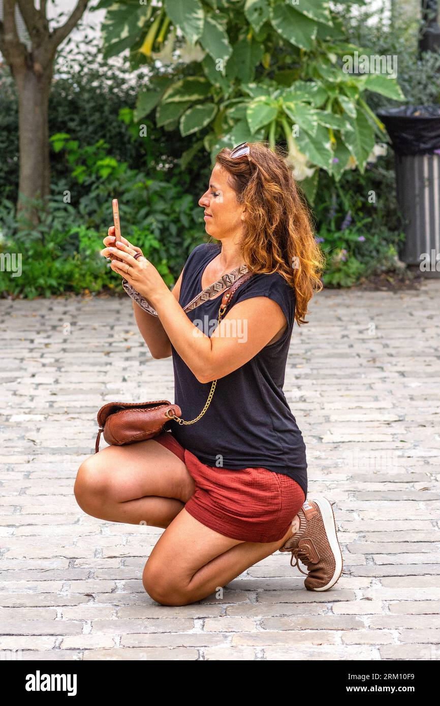 Junge Frau kniend Foto von Freunden mit Smartphone machen - Tours, Indre-et-Loire (37), Frankreich. Stockfoto