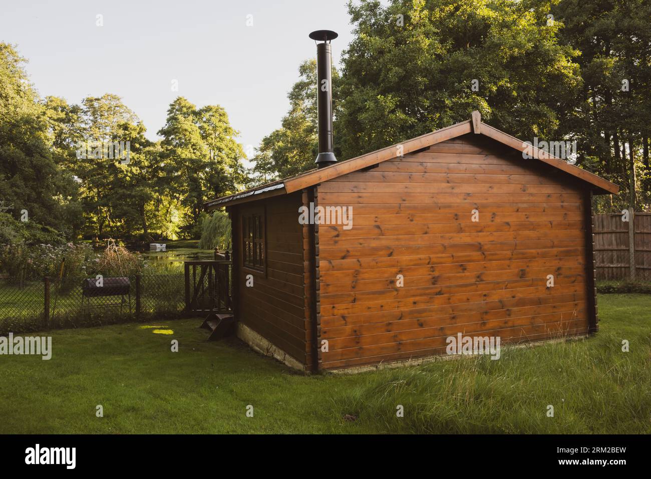 Ein hölzernes Sommerhaus mit einem Kamin aus Holz überblickt einen kleinen See in einem privaten Garten in Thetford, Norfolk, England Stockfoto
