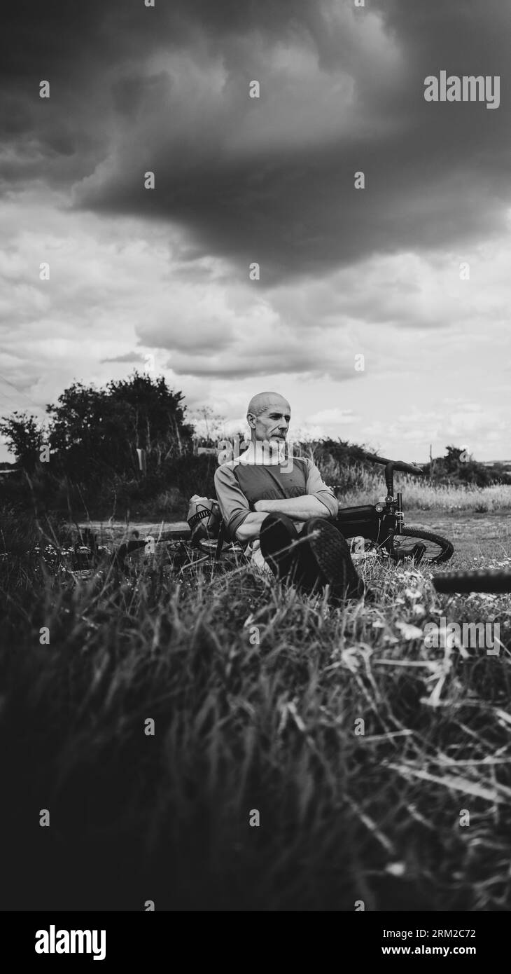 Ein kahlköpfiger Mann erholt sich vom Radfahren auf einem Bauernfeld, während sich Sturmwolken in der Nähe von Kings Lynn in Norfolk England sammeln Stockfoto