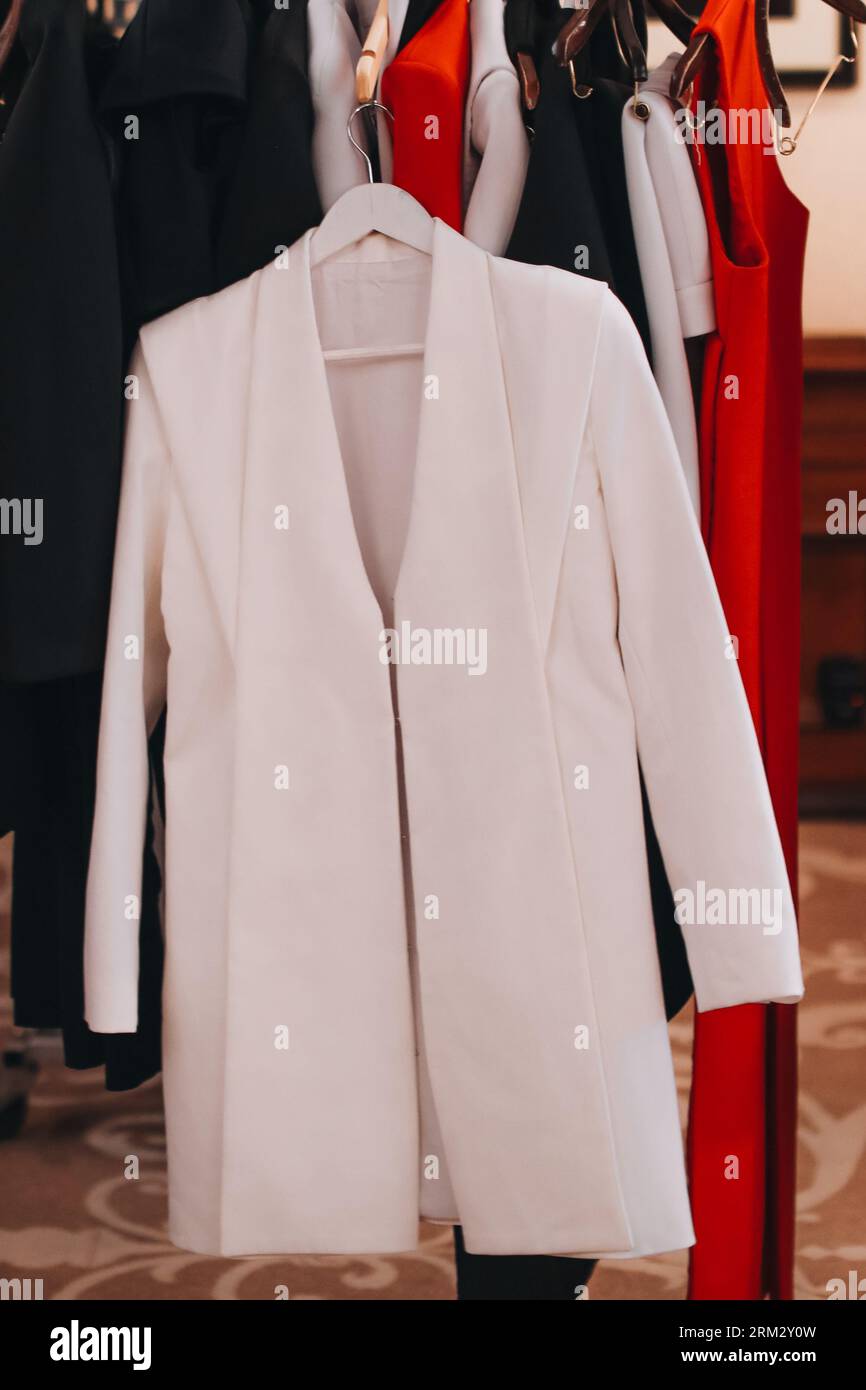 Weiße, elegante Damenjacke, die auf der modischen Backstage hängt. Vertikal Stockfoto