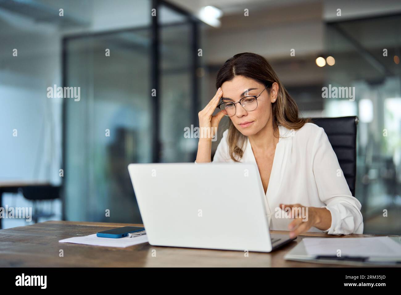 Besorgte, müde, reife Geschäftsfrau mit Brille und Kopfschmerzen bei der Arbeit. Stockfoto