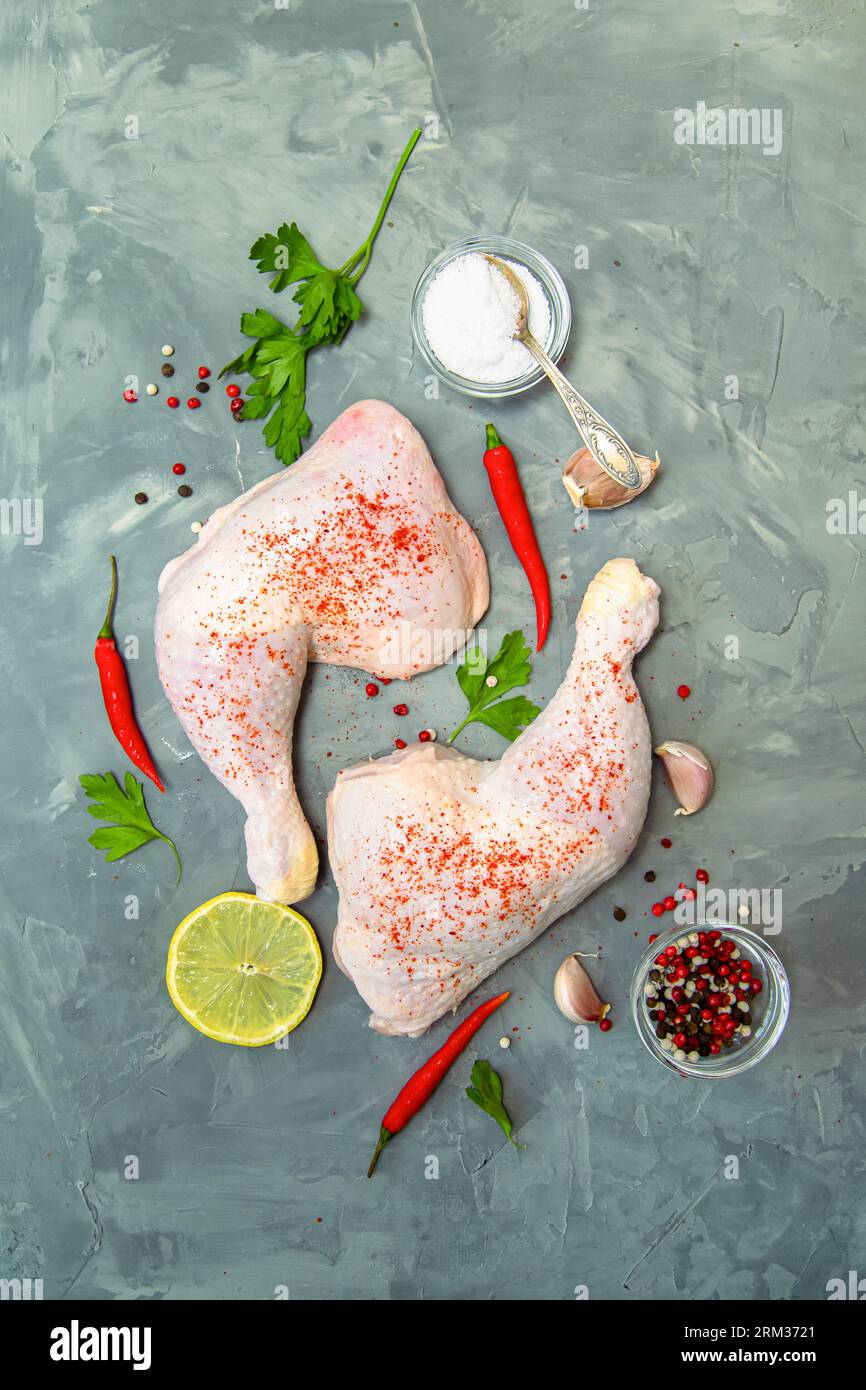 Rohe Hähnchenschenkel, Knoblauch, Chili, Zitrone und Kräuter auf grauem Hintergrund. Draufsicht. Stockfoto