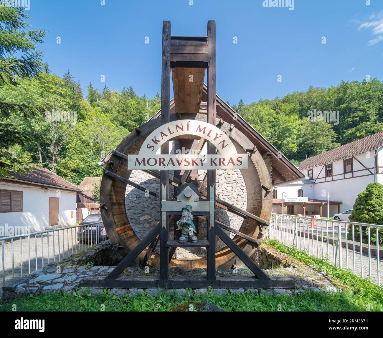 Vertikales oberschlächtiges Wassermühlenrad bei „Skalní mlýn“ (Felsmühle) mit einem Schild, das den Namen der Siedlung und die Vodnik-Statue angibt. Teil des Touristenzentrums. Stockfoto