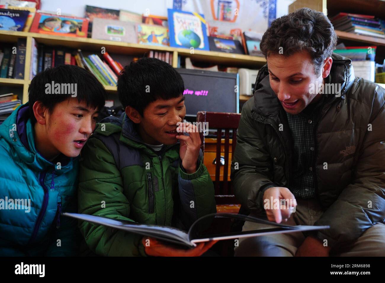 (131218) -- HUANGNAN, 17. Dezember 2013 (Xinhua) -- Andrew (R) liest ein Buch mit zwei Schülern an der Second Minzu Middle School in der tibetischen Autonomen Präfektur Huangnan, Provinz Qinghai im Nordwesten Chinas, 17. Dezember 2013. Der 29-jährige Andrew Frankel aus Amerika hat sich immer für die tibetische Kultur interessiert. 2012 verließ er seine Heimatstadt nach Qinghai und wurde Lehrer an der Schule. Neben dem Unterricht in Englisch gründete er eine englischsprachige Ecke und einen Filmclub, um eine bessere englischsprachige Atmosphäre für lokale Studenten zu schaffen. Ich liebe es, bei meinen Studenten zu bleiben, sagte Andrew Stockfoto