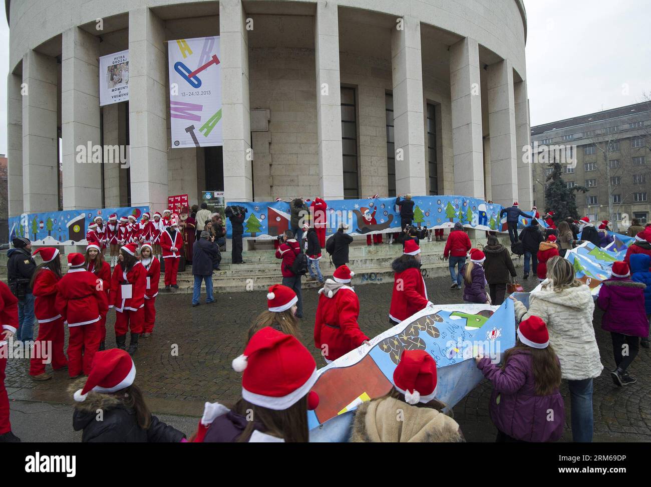 Junge Menschen, die als Weihnachtsmann gekleidet sind, tragen eine hundert Meter lange Weihnachtskarte durch die Innenstadt von Zagreb, Kroatien, am 21. Dezember 2013. Die riesige Weihnachtskarte mit den besten Wünschen der Menschen in Kroatien wird auf einer Weihnachtsmesse in Straßburg, Frankreich, ausgestellt. (Xinhua/Miso Lisanin)(yt) KROATIEN-ZAGREB-RIESIGE WEIHNACHTSKARTE PUBLICATIONxNOTxINxCHN Junge Prominente, die als Weihnachtsmann verkleidet sind, tragen eine 100 Meter lange Weihnachtskarte durch die Innenstadt von Zagreb Kroatien 21. Dezember 2013 die große Weihnachtskarte mit den besten Wünschen der Prominenten Kroatiens wird IN A C ausgestellt Stockfoto