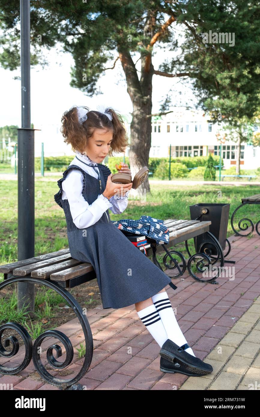 Mädchen mit Rucksack, das Sandwich in einer Sandwichbox in der Nähe der Schule isst. Ein schneller Snack mit einem Brötchen, ungesundes Essen, Mittagessen aus der Schule. Zurück zur Schule. Stockfoto