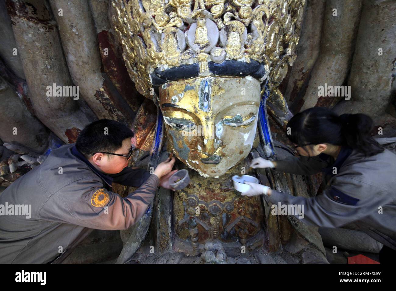 (140318) -- CHONGQING, 18. März 2014 (Xinhua) -- Mitarbeiter entfernen sich von der Skulptur von Qianshou Guanyin (Bodhisattva mit tausend Händen) auf dem Mount Baoding im Bezirk Dazu in der Gemeinde Chongqing im Südwesten Chinas, 18. März 2014. Die Skulptur, die in der 7,7 Meter hohen und 12,5 Meter breiten Höhle geschnitzt wurde, könnte auf die Southern Song Dynastie (1127 bis 1279) zurückgehen. Im Laufe der Jahrhunderte ist die Farbe der Skulptur verblasst, Teile der Goldfolie haben sich abgelöst und Risse sind aufgetaucht. Und so wurde ein Restaurierungsprojekt für die buddhistische Statue gestartet Stockfoto