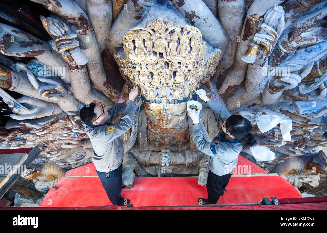 (140318) -- CHONGQING, 18. März 2014 (Xinhua) -- Mitarbeiter entfernen sich von der Skulptur von Qianshou Guanyin (Bodhisattva mit tausend Händen) auf dem Mount Baoding im Bezirk Dazu in der Gemeinde Chongqing im Südwesten Chinas, 18. März 2014. Die Skulptur, die in der 7,7 Meter hohen und 12,5 Meter breiten Höhle geschnitzt wurde, könnte auf die Southern Song Dynastie (1127 bis 1279) zurückgehen. Im Laufe der Jahrhunderte ist die Farbe der Skulptur verblasst, Teile der Goldfolie haben sich abgelöst und Risse sind aufgetaucht. Und so wurde ein Restaurierungsprojekt für die buddhistische Statue gestartet Stockfoto