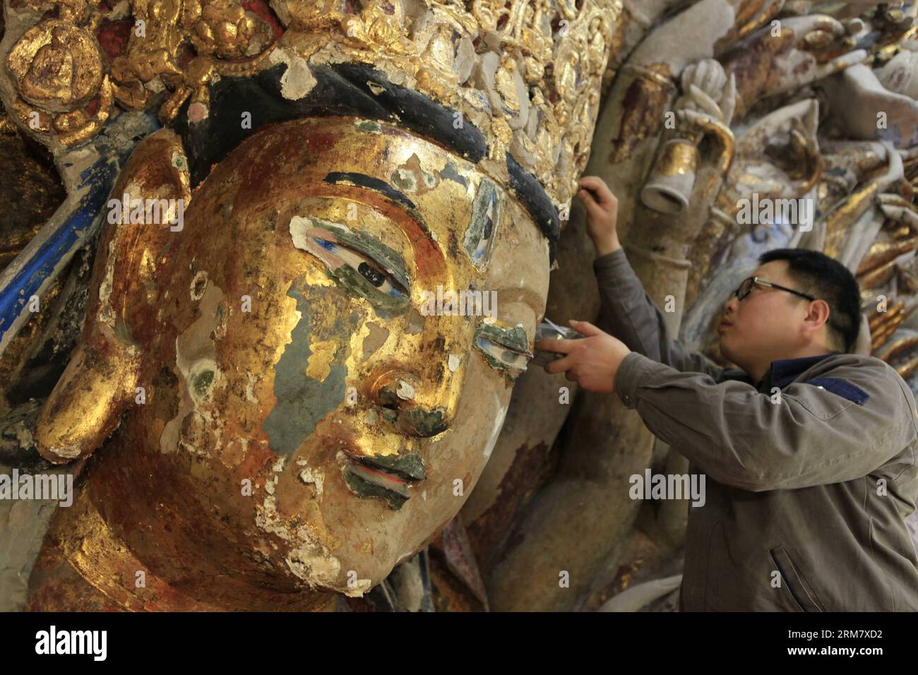 (140318) -- CHONGQING, 18. März 2014 (Xinhua) -- Ein Mitarbeiter entfernt die abblätternde Goldfolie von der Skulptur von Qianshou Guanyin (Bodhisattva mit tausend Händen) auf dem Mount Baoding im Bezirk Dazu in der Gemeinde Chongqing im Südwesten Chinas, 18. März 2014. Die Skulptur, die in der 7,7 Meter hohen und 12,5 Meter breiten Höhle geschnitzt wurde, könnte auf die Southern Song Dynastie (1127 bis 1279) zurückgehen. Im Laufe der Jahrhunderte ist die Farbe der Skulptur verblasst, Teile der Goldfolie haben sich abgelöst und Risse sind aufgetaucht. Und so wurde ein Restaurierungsprojekt für die buddhistische Statue gestartet Stockfoto