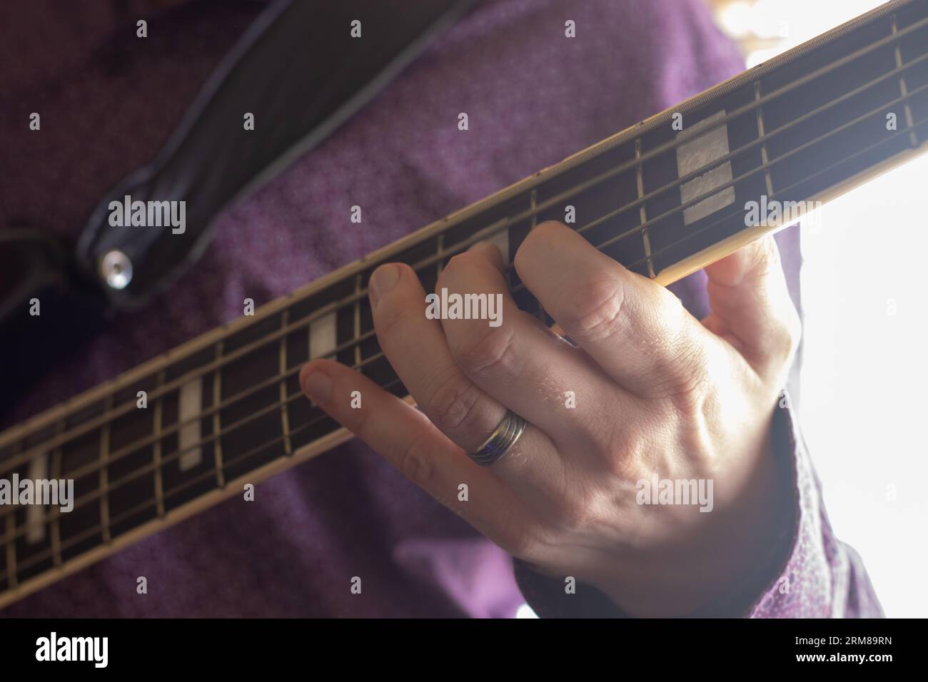 Nahaufnahme eines Mannes mit violettem Hemd, der eine Basisgitarre spielt Stockfoto