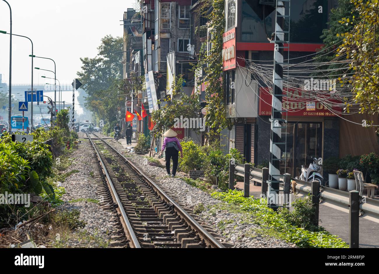 Eine ältere vietnamesische Frau mit einem konischen Hut spaziert entlang der Nord-Süd-Hauptbahn neben dem Highway One in Hanoi, Vietnam. Es ist ein sonniger Tag Stockfoto