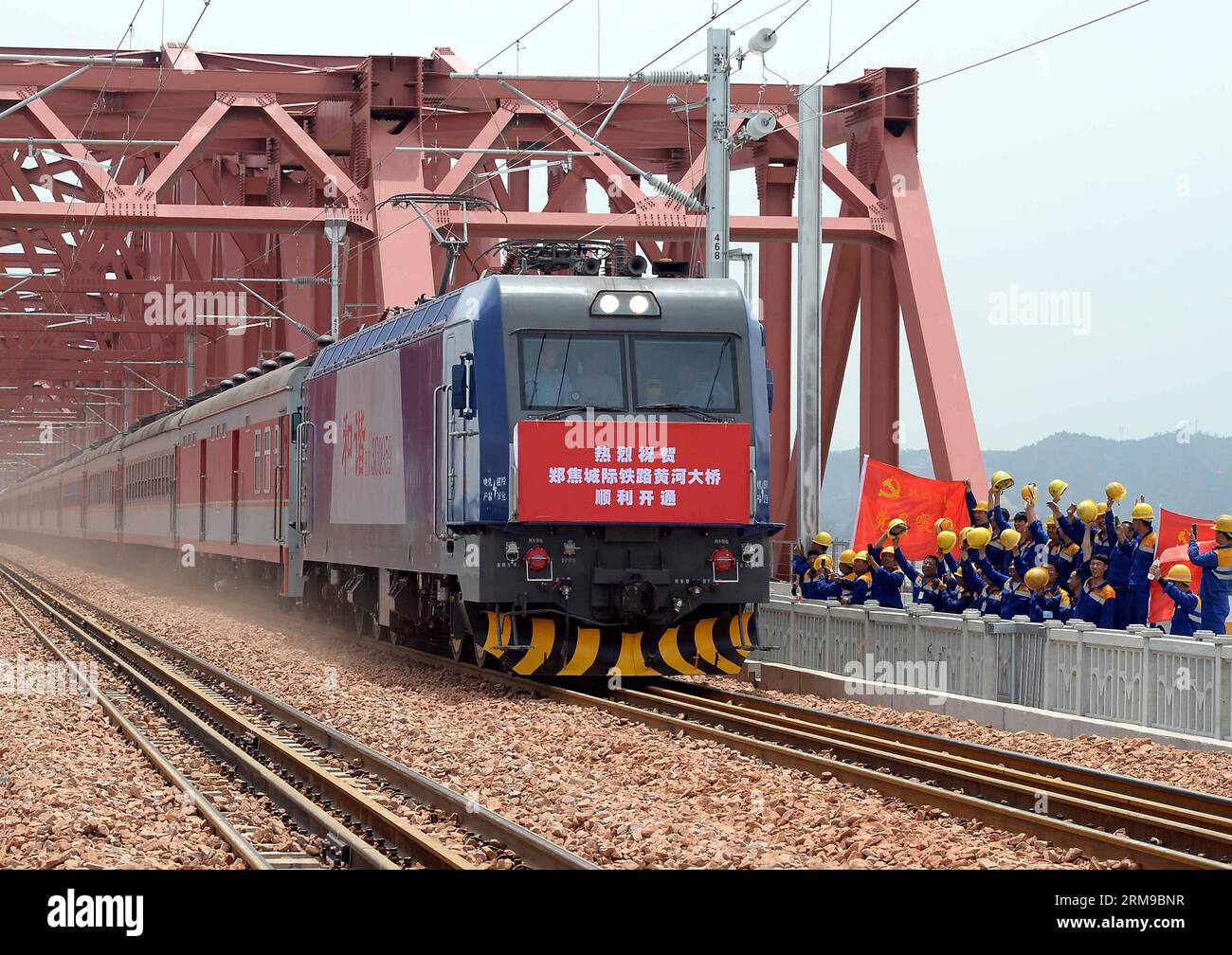 Die Arbeiter jubeln, als der erste Personenzug am 16. Mai 2014 durch eine neue Brücke über den Gelben Fluss in Zhengzhou, der Hauptstadt der zentralchinesischen Provinz Henan, fährt. Die erste vierspurige Eisenbahnbrücke über den Gelben Fluss, Chinas zweitlängste Brücke, wurde am Freitag in Betrieb genommen und ersetzte eine zweispurige Konstruktion, die seit 1960 in Betrieb war. Zwei Linien der 2.200 Meter langen Brücke sind für die Peking-Guangzhou-Eisenbahn, die anderen zwei für Überlandzüge zwischen Zhengzhou und Jiaozuo, einer Stadt in Henan. (Xinhua/Wang Song) (wf) CHINA-HENAN-ZHENGZHOU-YELLOW RIVER-RAILWAY BRIDGE (CN) PUB Stockfoto