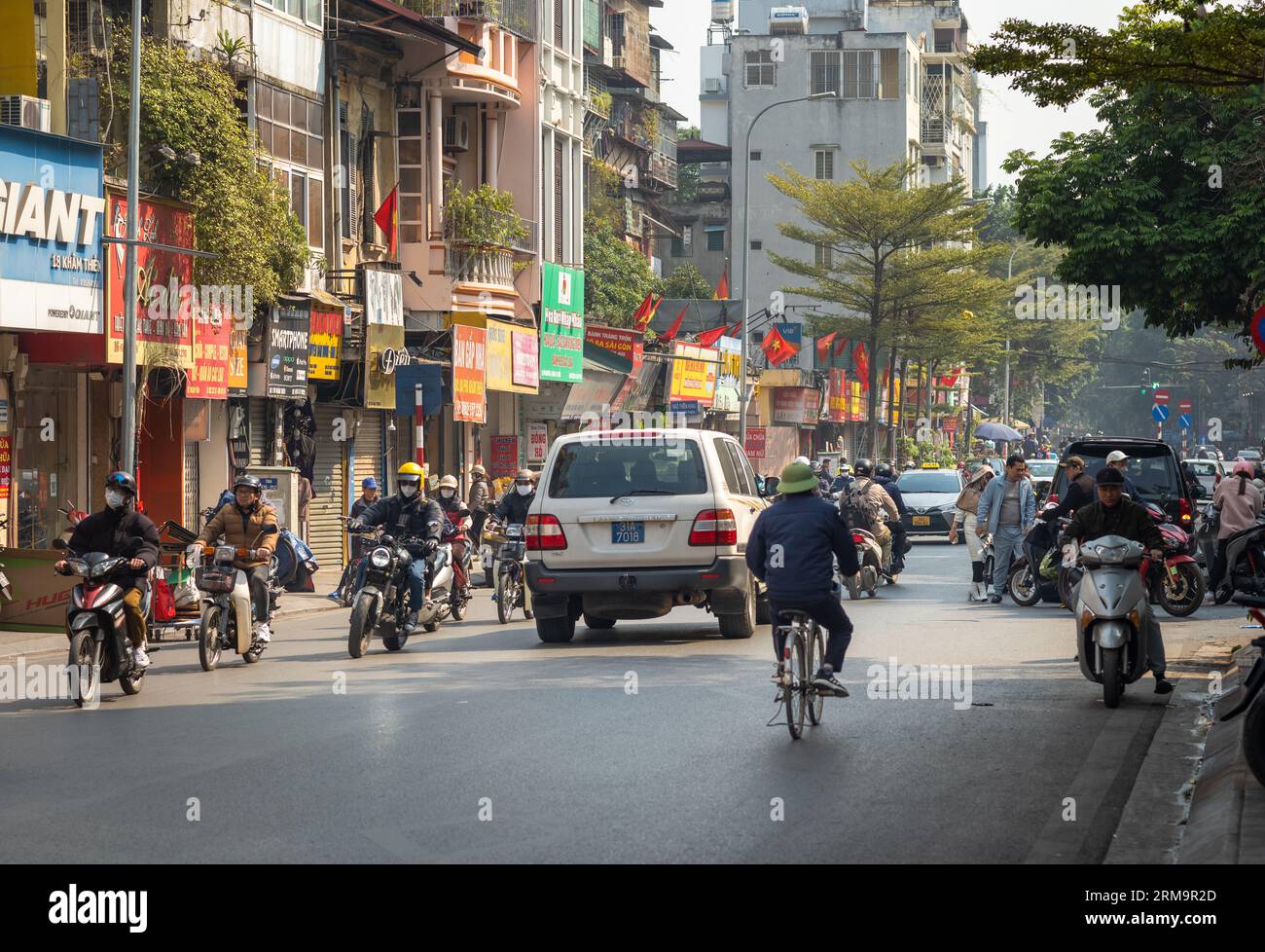 Ein vietnamesischer Mann, der einen traditionellen grünen Armt-Pith-Helm trägt, radelt im schweren und chaotischen Verkehr an Geschäften entlang der Kham Thien Street in Hanoi, Vietnam Stockfoto