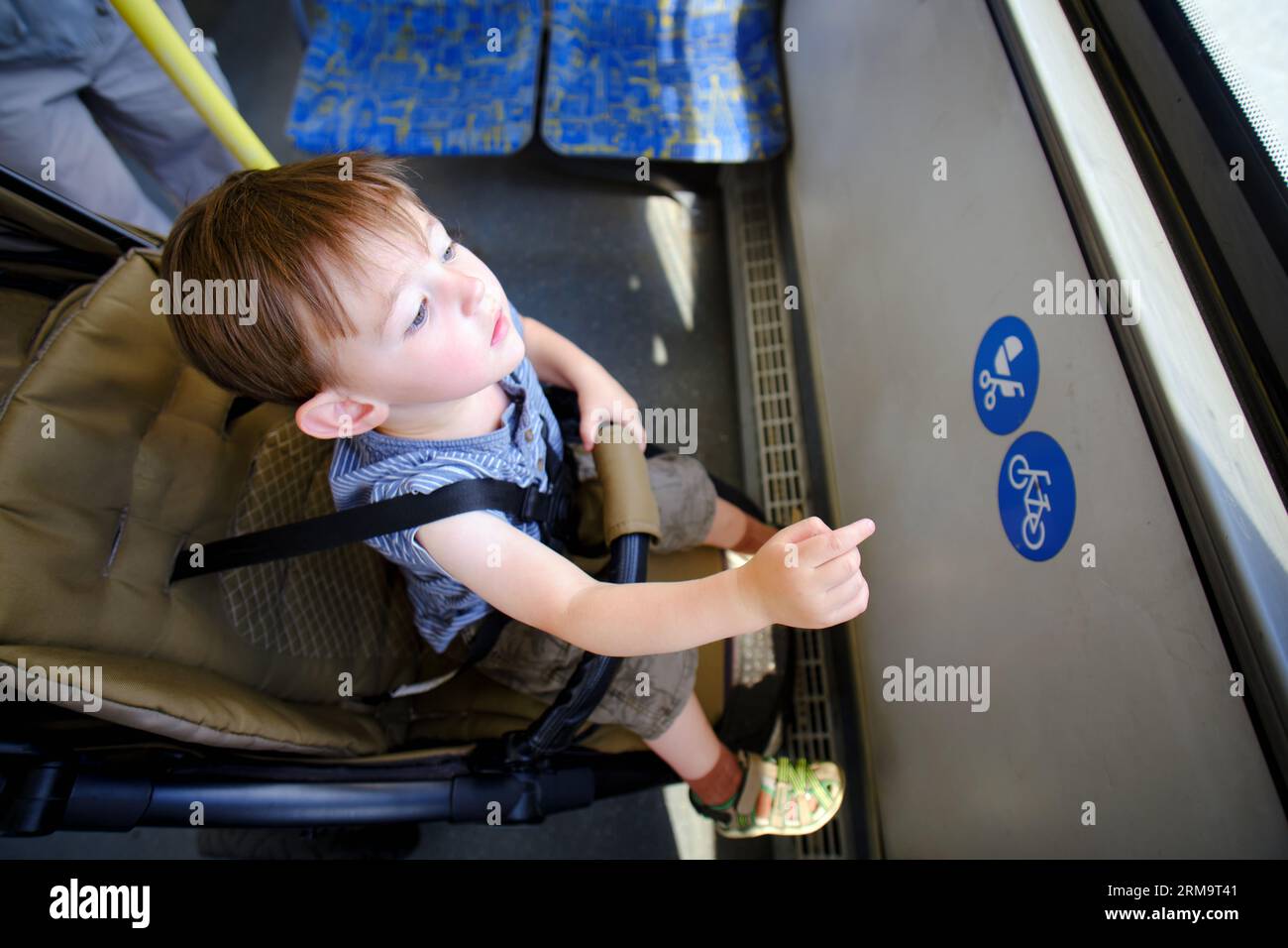 Das Kleinkind sitzt in einem Kinderwagen im Bus, und die Leute gehen draußen vorbei. Junge im Alter von zwei Jahren (zwei Jahre) Stockfoto