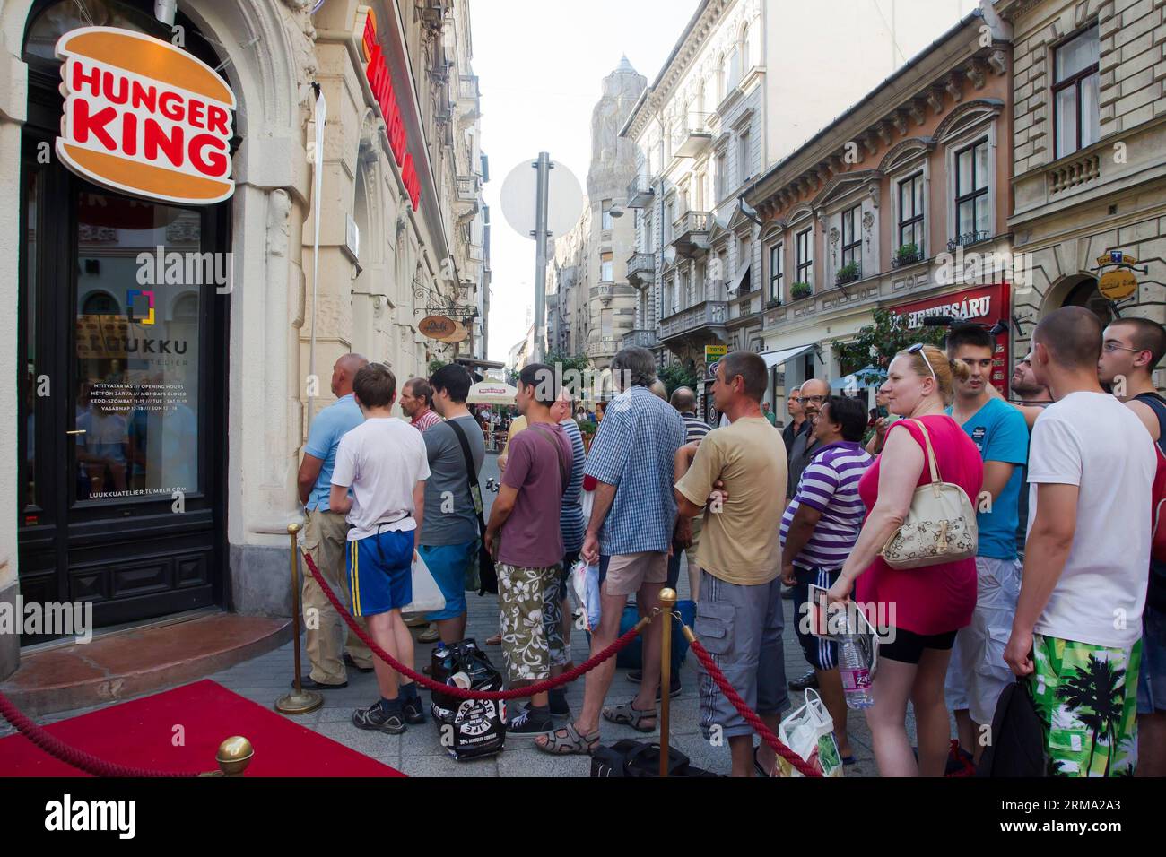 BUDAPEST, 11. Juni 2014 (Xinhua) -- die Menschen stehen in der Warteschlange für kostenloses Geld, das in Hamburger-Boxen für arme Menschen im Rahmen des Hunger King-Projekts der finnischen Künstlerin Jani Leinonen in Budapest, Ungarn, am 11. Juni 2014 serviert wird. Jani Leinonen eröffnete am Mittwoch in Budapest einen gefälschten Imbissladen mit einem ähnlichen Design wie Burger King. Sein Projekt zielt darauf ab, das Bewusstsein für Armut in Ungarn zu schärfen. Das Hunger King-Projekt bietet armen Menschen, die bereit sind, stundenlang neben dem roten Karpfen in der Schlange zu stehen, kostenloses Geld (3400 ungarische Forint, das entspricht dem täglichen Teil des offiziellen Mindestlohns in Ungarn) Stockfoto