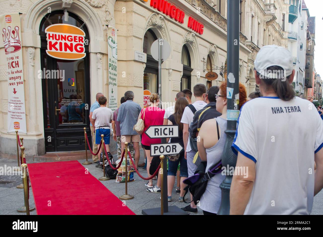 BUDAPEST, 11. Juni 2014 (Xinhua) -- die Menschen stehen in der Warteschlange für kostenloses Geld, das in Hamburger-Boxen für arme Menschen im Rahmen des Hunger King-Projekts der finnischen Künstlerin Jani Leinonen in Budapest, Ungarn, am 11. Juni 2014 serviert wird. Jani Leinonen eröffnete am Mittwoch in Budapest einen gefälschten Imbissladen mit einem ähnlichen Design wie Burger King. Sein Projekt zielt darauf ab, das Bewusstsein für Armut in Ungarn zu schärfen. Das Hunger King-Projekt bietet armen Menschen, die bereit sind, stundenlang neben dem roten Karpfen in der Schlange zu stehen, kostenloses Geld (3400 ungarische Forint, das entspricht dem täglichen Teil des offiziellen Mindestlohns in Ungarn) Stockfoto