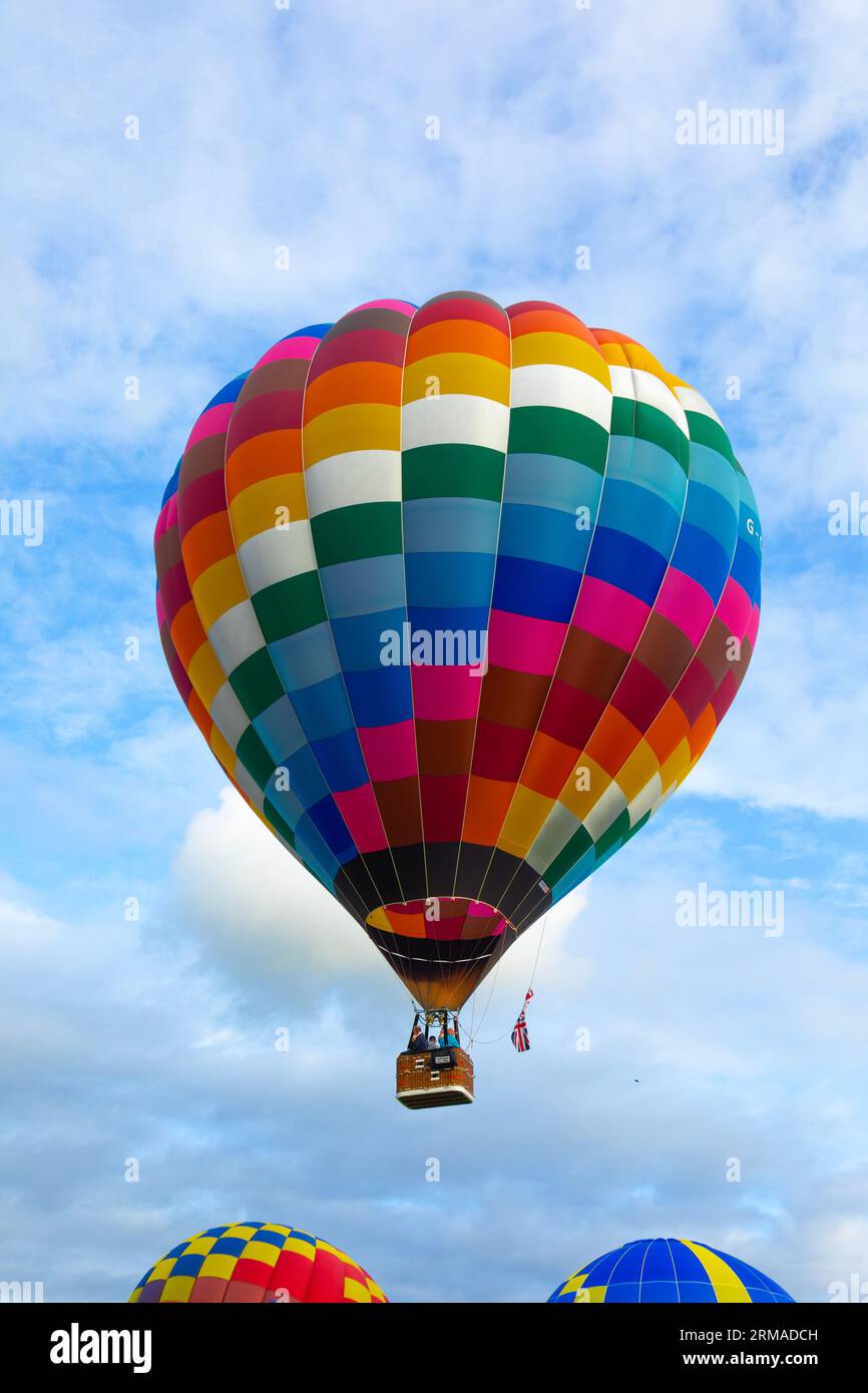 Ein Heißluftballon mit Fluggästen, die während des Strathaven Balloon Festivals 2023 in Strathaven, Schottland, über zwei anderen Ballons starten Stockfoto