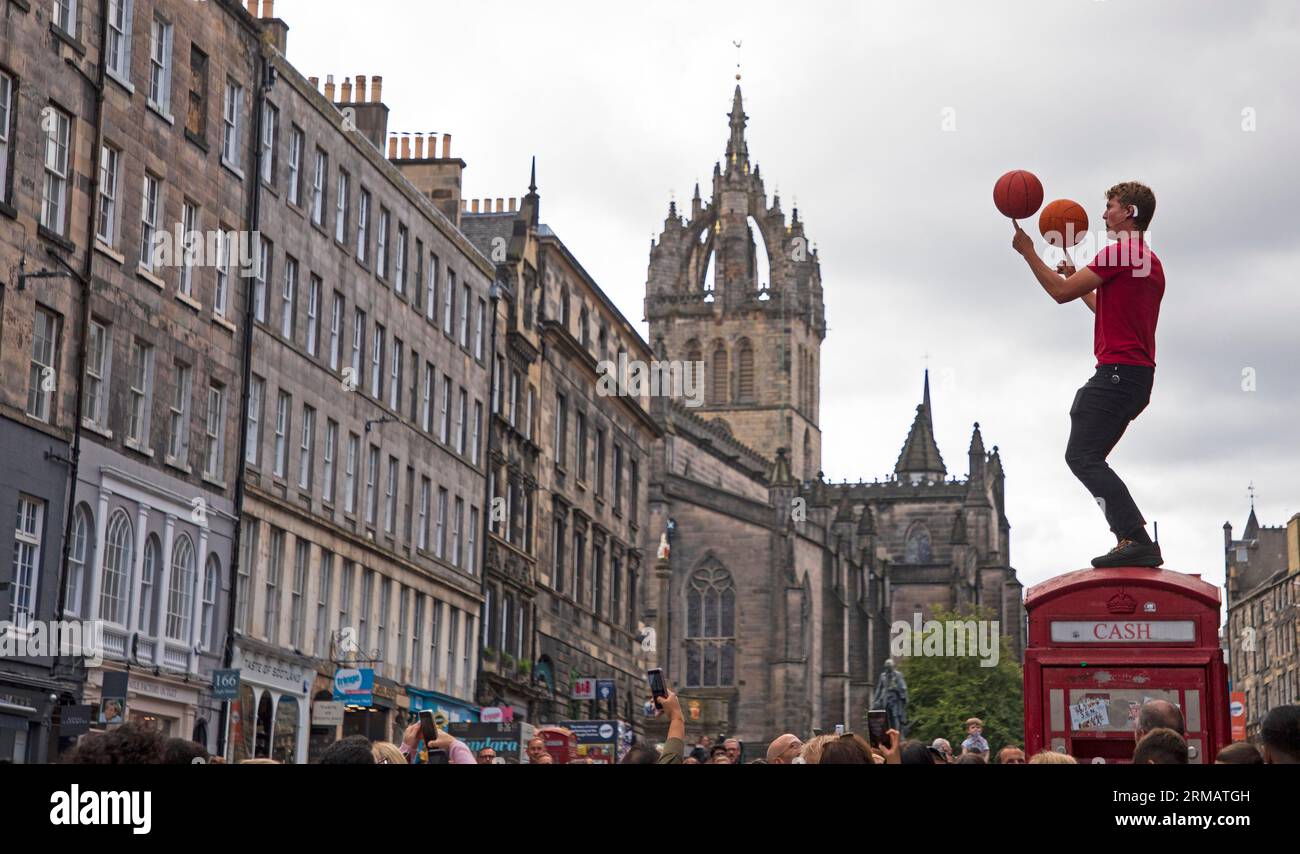 Royal Mile, Edinburgh, Schottland, Großbritannien. 27. August 2023. Obwohl das offizielle Edinburgh Festival Fringe am Montag, den 28. August endet, gab es auf der High Street keine Sicherheits- oder Fringe-Mitarbeiter, um die Massen und die Zeit der Straßenkünstler zu überwachen. Es gab jedoch immer noch große Zuschauergruppen, die sich zur Unterhaltung versammelten. Hunter aus Hawaii demonstriert sein Können mit Basketballen am Finger, während er auf einem ehemaligen Telefonkiosk sitzt. Quelle: Arch White/Alamy Live News. Stockfoto