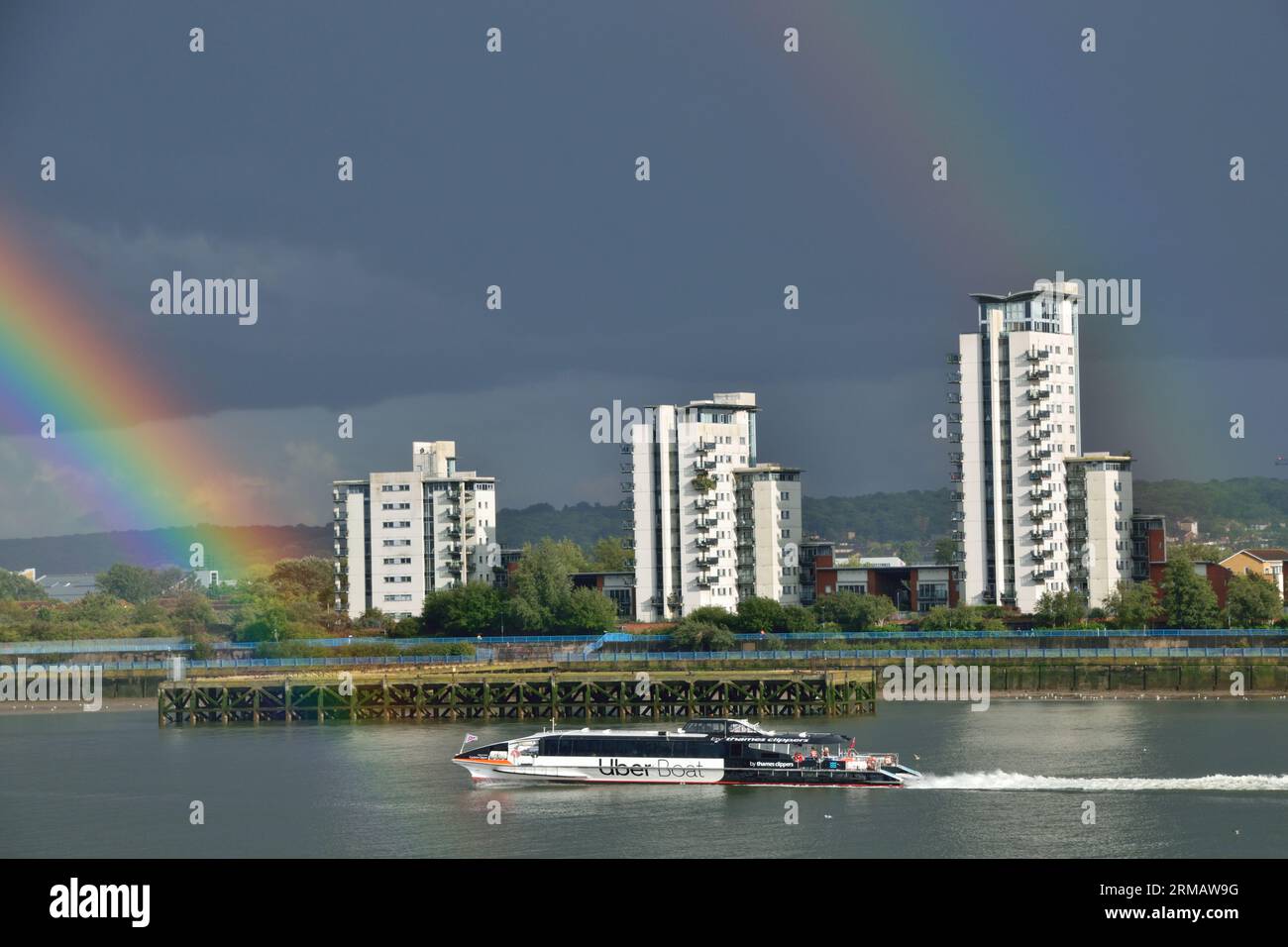 Uber Boat by Thames Clipper River Bus Service-Schiff Cyclone Clipper on the River Thames in London unter Sturm mit einem Regenbogen Stockfoto