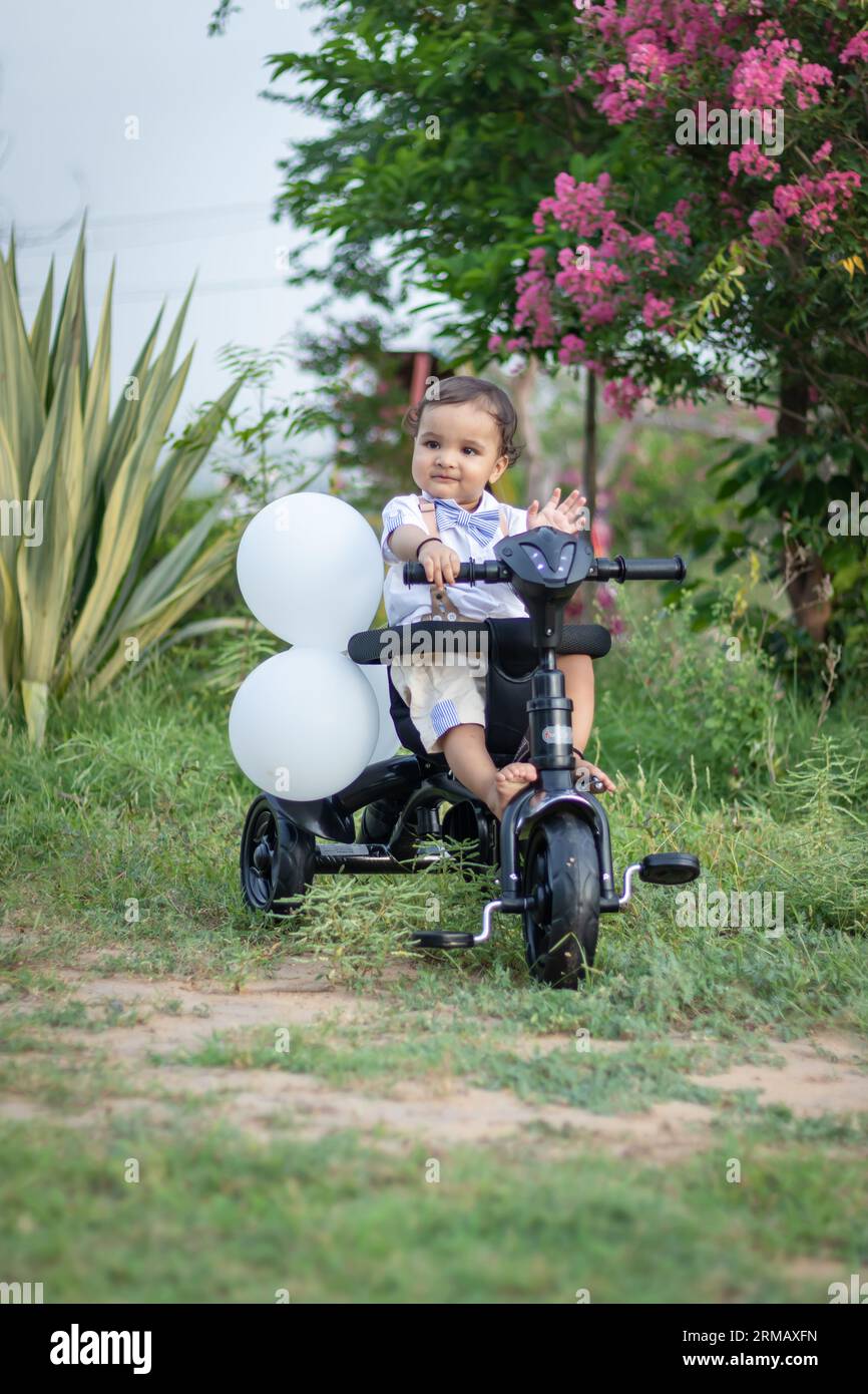 Isoliertes, süßes Kleinkind mit unschuldigem Gesichtsausdruck auf dem Dreirad im Freien aus verschiedenen Blickwinkeln Stockfoto
