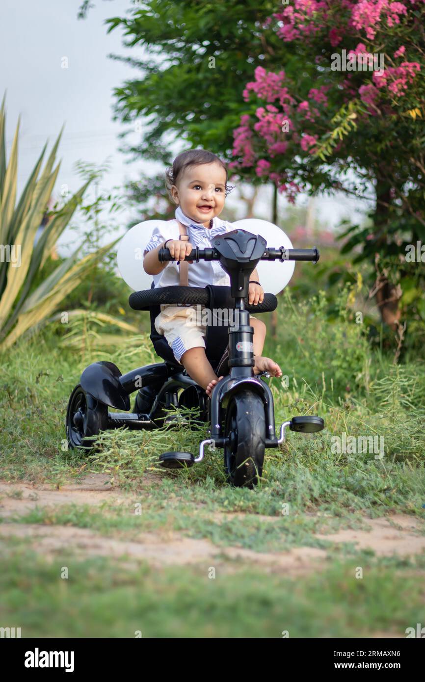 Isoliertes, süßes Kleinkind mit unschuldigem Gesichtsausdruck auf dem Dreirad im Freien aus verschiedenen Blickwinkeln Stockfoto