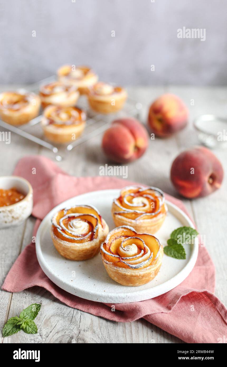 Nektarinenrosen aus Blätterteig, auf einer weißen Platte. Buttrige, flakige und knusprige Blätterteigrollen mit Schichten aromatischer Nektarinscheiben. Pinkfarbenes Nickerchen Stockfoto