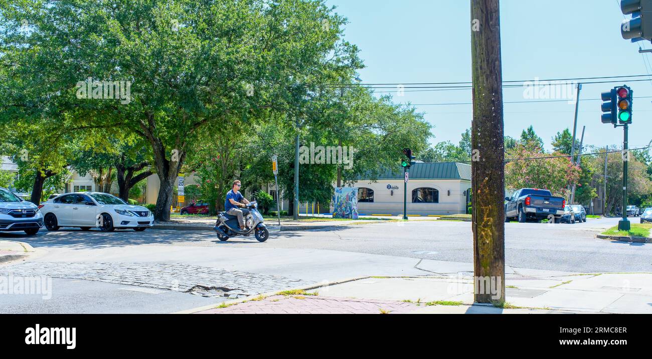 NEW ORLEANS, LA, USA - 19. AUGUST 2023: Ein Mann ohne Helm fährt an einer Kreuzung während der Hauptverkehrszeit ein rotes Licht auf seinem Motorroller Stockfoto